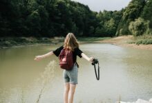 Hiker and a Camera Standing by a Lake in the Forest with Her Arms Spread अकेली घूमने की सोच रही हैं? भारत में ये 9 यात्रा स्थल हैं सबसे बेहतरीन